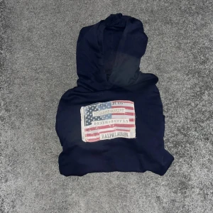 Mörkblå hoodie från Ralph Lauren - Säljer en snygg mörkblå hoodie från Ralph Lauren med ett stort amerikanskt flaggmotiv på bröstet. Unik och väldigt stilren. 