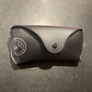 Svarta solglasögon från Ray-Ban - Snygga svarta Ray-Ban solglasögon med polariserade linser. Modellen är RB 8313 och har en klassisk aviator-stil. Perfekta för att skydda ögonen med stil. Kommer med ett stilrent fodral.