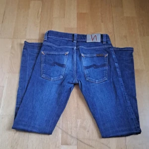 Blå jeans från Nudie Jeans - Snygga blå jeans från Nudie Jeans med klassisk femficksdesign och orange sömmar. De har en knappgylf och är tillverkade i slitstarkt denim. Perfekta för en stilren look. 10-10 skick dem är inprincip helt nya. 