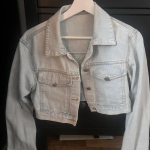 Ljusblå croppad jeansjacka - Snygg ljusblå croppad jeansjacka med knappar framtill och två bröstfickor. Perfekt för en avslappnad stil. Jackan har långa ärmar och en klassisk krage.