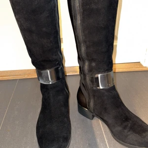 Svarta stövlar från Calvin Klein - Snygga svarta stövlar från Calvin Klein i mocka med dragkedja och metallspänne. Över knä höjd, storlek 39 knappt använda! 