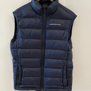 Mörkblå dunväst från Peak Performance - Säljer en snygg mörkblå dunväst från Peak Performance. Västen har en dragkedja framtill och är perfekt för kyligare dagar. Den är stilren och lätt att matcha med andra plagg.