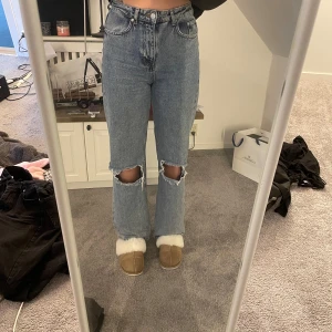 Blå jeans med slitna knän från NA-KD - Säljer ett par blå jeans från NA-KD med slitna detaljer vid knäna. De har en klassisk femficksdesign och är tillverkade i ett robust denimtyg. Perfekta för en avslappnad stil.