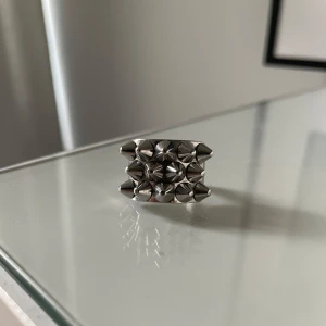 Silvrig ring med nitar - Cool och edgy ring i silver med flera rader av spetsiga nitar. Perfekt för att ge din outfit en tuffare look. Passar bra till både vardag och speciella tillfällen.