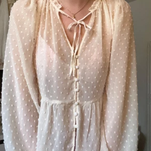 Söt blus från Zara - Vit/beige Blus från Zara i storlek S. Mönster med ”prickar” samt knappar längst med blusen och knytning vid hals och ärm. Använd ett fåtal gånger, inga defekter.