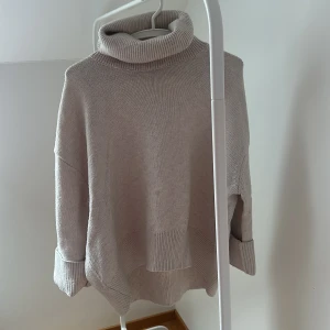 Beige polotröja från H&M - Mysig beige polotröja från H&M i stickat material. Perfekt för kyliga dagar med sin höga krage och långa ärmar. Tröjan har en avslappnad passform och ribbade detaljer vid ärmslut och nederkant.