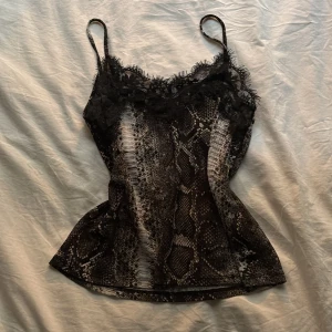 Ormmönstrad linne från Zara - Snygg ormmönstrad linne från Zara med spetsdetaljer vid halsringningen. Linnet har smala axelband och en figurnära passform. Perfekt för en trendig look eller fest.