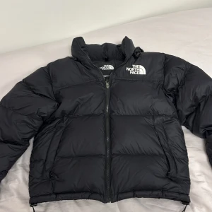 North Face puffer - Säljer en svart dunjacka från The North Face. Jackan har en dragkedja framtill och är långärmad med en pufferdesign. Perfekt för kalla dagar med sin varma och isolerande stil. Logotypen är synlig både fram och bak.