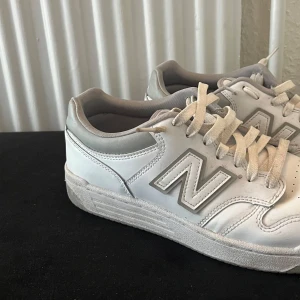 Vita sneakers från New Balance - Säljer ett par vita New Balance sneakers med klassisk design och snörning. Skorna har en stilren look med märkets logga på sidan och baksidan. Perfekta för en avslappnad stil.