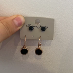 Svarta örhängen med guldfärgad kant - Snygga svarta örhängen med guldfärgad kant. Setet innehåller både små knappar och hängande örhängen. Perfekt för att ge en elegant touch till din outfit.