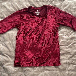 Vinröd sammetstopp från Pepperts - Säljer en snygg vinröd topp från Pepperts. Toppen har trekvartsärmar och en mjuk, glansig yta som ger en lyxig känsla. Perfekt för att lägga till lite glamour i vardagen. Passar åldrar 10-12 år.
