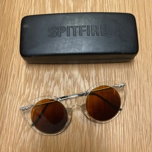 Transparenta solglasögon från Spitfire - Snygga transparenta solglasögon från Spitfire med bruna linser. Kommer med ett svart fodral, fodret i fodralet har lossnat men säker förvaring. Någon liten repa på linsen men annars topp!