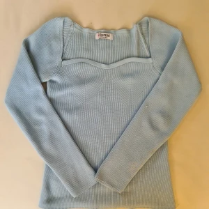 Ljusblå ribbad tröja från Esperi - Snygg ljusblå ribbad tröja från Esperi med långärmad design. Tröjan har en unik skärning vid halsen som ger en modern look. Perfekt för kyligare dagar.