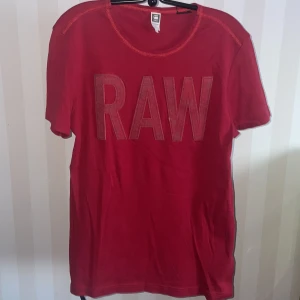 Röd t-shirt från G-Star RAW - Snygg röd t-shirt från G-Star RAW med stort 'RAW' tryck på framsidan. Perfekt för en casual look. Kortärmad och tillverkad i mjukt material för extra komfort.