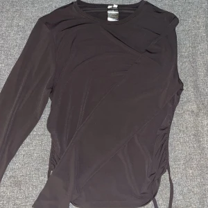 Svart långärmad topp från nelly - Snygg svart långärmad topp från nelly med dragsko-detaljer på sidorna. Öppen i ryggen där man kan knyta