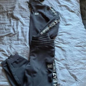 Svart dress från EA7 - Dress från EA7 med logotyp längs benet. Perfekta och ärmarna. för en avslappnad stil med elastisk midja och ribbade muddar vid bensluten. Text på arm och ben är Reflex, passar strl S