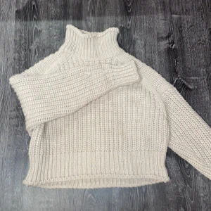 Beige stickad polotröja från H&M - Mysig beige stickad polotröja från H&M. Perfekt för kyliga dagar med sin höga krage och ribbade detaljer. Tröjan har en croppad passform som ger en modern look.