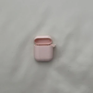Rosa fodral för hörlurar - Säljer ett sött rosa fodral för trådlösa hörlurar. Fodralet har en smidig öppning och en liten ögla för att fästa en rem eller nyckelring. Perfekt för att skydda dina hörlurar och hålla dem stiliga.