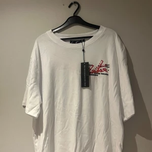 Vit t-shirt med tryck - Vit t-shirt med tryck i rött och svart på både fram- och baksidan. T-shirten har en avslappnad passform och korta ärmar. Perfekt för en casual look.