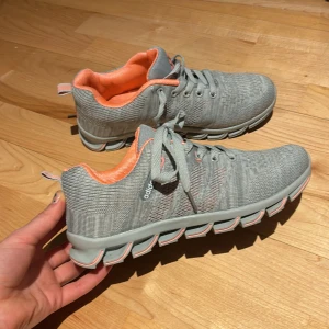 Grå och orange sneakers från Adidas  - Snygga grå sneakers från Adidas med orange insida och snörning. Skorna har en unik sula med bra grepp och är perfekta för en aktiv livsstil. Adidas-loggan syns tydligt på sidan. Mycket mycket bra kvalite eftersom den nästan aldrig är använd! PRIS kan diskuteras!