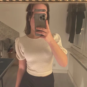 Vit ribbad topp med knytband - Säljer en stilren vit ribbad topp med korta puffärmar och knytband i ryggen från Gina. Toppen är croppad och har en öppen rygg som ger en trendig look. Perfekt för både vardag och fest!