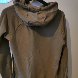 Beige hoodie från Nike - Säljer en snygg beige hoodie från Nike med klassisk logga på bröstet. Tröjan har en stor ficka framtill och justerbar huva med dragsko. Perfekt för en avslappnad stil.