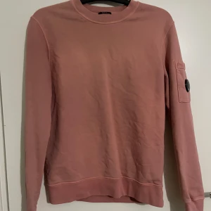Rosa sweatshirt med detalj på ärmen / gruby sweter  - En ljusrosa tjock tröja med en rund "skiva" på armen där det står ( C.P. COMPANY ) plasten är kvar på tröjan då jag aldrig har haft på mig den. Färgen är absolut inte lika blek i verkligheten som den är i bilden, färgen är mer tydlig. Jag är 155 och den går ner för rumpan på mig så den är ganska lång den är 100% äkta om fler bilder önskas skriv bara!  ( köparen står för frakt! ) 