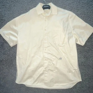 Beige kortärmad skjorta  - Säljer en stilren beige kortärmad skjorta. Skjortan har en klassisk krage och knappar framtill. Perfekt för en avslappnad stil.