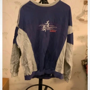 Blå och grå tröja från Adidas - Säljer en blå och grå tröja från Adidas med ett coolt tryck på framsidan. Tröjan har långa ärmar och en avslappnad passform. Perfekt för en sportig look eller en chill dag. Kan gå ner i pris!! Finns några defekter, men är annars bra. Ställ gärna frågor kring defekterna om intresserad av varan!