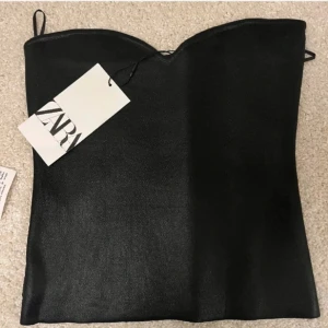 Svart tubtopp från Zara - Snygg svart tubtopp från Zara i ett glansigt material. Säljer pågrund av att den är för liten