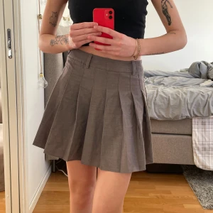 Grå plisserad kjol - Snygg grå plisserad kjol med hög midja och bälteshällor. Perfekt för en stilren look. Kjolen har en kort längd och ger en klassisk touch till din outfit. Endast använd två gånger✨