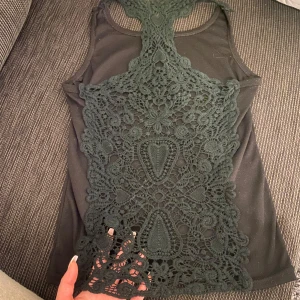 Svart linne med spetsdetaljer - Snyggt svart linne med vackra spetsdetaljer på baksidan. Perfekt för en stilren och elegant look. Linnet är ärmlöst och har en unik design med spetsmönster som ger en extra touch. Finns inga lappar i tröjan men jag skulle uppskatta tröjan som en S.