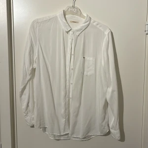 Vit skjorta från Lee - Säljer en klassisk vit skjorta från Lee i storlek S. Skjortan har långa ärmar och en bröstficka med diskret logga. Perfekt för en stilren look. Knappar framtill ger en tidlös design.