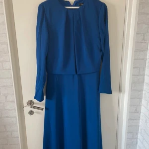 Modest blå elegant långklänning - Elegant blå långklänning med långärmad design och en stilfull öppen rygg- och fram med svart och silver detslj under som gör den modest. Perfekt för speciella tillfällen. Strl 44 MEN passar strl 40 och 42!!. Använt en gång så den är fortfarande i väldigt bra skick.