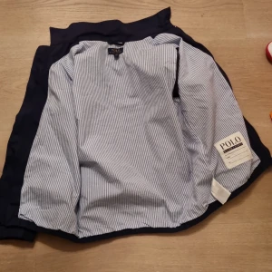 Randig vårjacka från Polo Ralph Lauren - Säljer en stilren blå- och vitrandig sommar/vårjacka från Polo Ralph Lauren. Skjortan har långa ärmar och är tillverkad i ett mjukt bomullsmaterial. Perfekt för en klassisk och avslappnad look. Storken är 14-16 vilket motsvarar xs/xxs