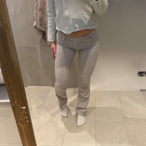 Grå randiga byxor - Snygga grå byxor med vita ränder. De är lågmidjade och har en tight passform som framhäver figuren. Perfekta för en stilren look.