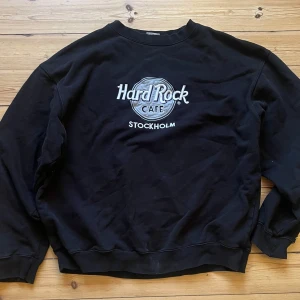 Svart Hard Rock Cafe sweatshirt - Säljer en svart sweatshirt från Hard Rock Cafe med Stockholm-tryck på framsidan. Tröjan har långa ärmar och en klassisk rund halsringning. Perfekt för en avslappnad stil. 