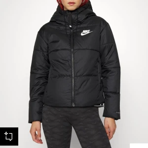 Svart pufferjacka från Nike - Snygg svart pufferjacka från Nike med huva och dragkedja. Perfekt för kyliga dagar med sin vadderade design. Jackan har en normal passform och är långärmad.