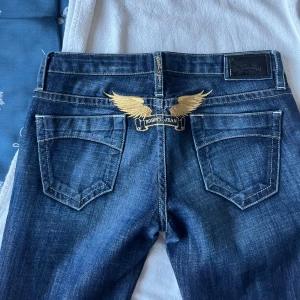 Mörkblå ’Robins Jean’ med guldbroderi - Snygga mörkblå jeans med ett väldigt unikt guldbroderi av vingar på bakfickan. Från ett Amerikanskt märke som heter Robins Jean. Bootcut modell och låg midja. Strl W26. Pm för mått/mer info💞Nypris runt 2000. Kolla gärna in de andra jeansen i min profil! 