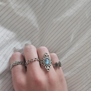 Set med silverringar och blå sten - Säljer ett set med fyra unika silverringar. En av ringarna har en stor blå sten i mitten med detaljerade mönster runtomkring, perfekt för att ge en touch till din outfit. De andra två ringarna har stjärn- och blommönstriga.❤️❤️
