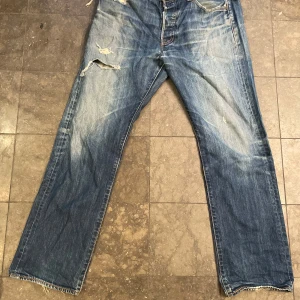 Levis 501 jeans i blå denim - Säljer ett par klassiska Levis 501 jeans i blå denim. De har en vintage look med slitningar och fransiga kanter med nice wash.