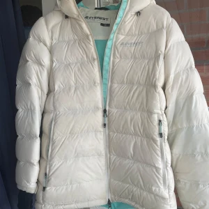 Vit dunjacka från Everest - Säljer en supermysig vit dunjacka från Everest. Den är perfekt för kalla vinterdagar med sin tjocka vaddering och långa ärmar. Jackan har en praktisk dragkedja och en skön huva för extra värme. Den är i storlek 40 och passar perfekt för vinterns alla äventyr!