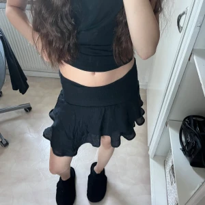 Svart volangkjol - Säljer en superfin svart volangkjol som är perfekt för både vardag och fest. Kjolen har en elastisk midja som gör den bekväm och lätt att bära. Den är kort och har flera lager av volanger som ger en snygg och lekfull look. Passar perfekt till en somrig outfit eller en kväll ute!