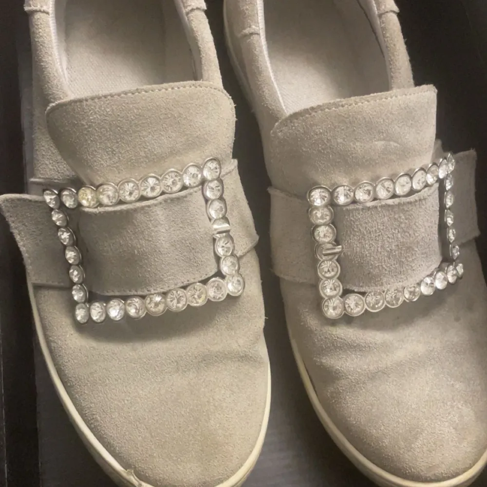 Säljer ett par snygga beige loafers i mocka med glittrande strassdetaljer på ovansidan. Perfekta för att ge en touch av glamour till vardagsoutfiten. De är i bra skick och kommer i originalkartong.. Skor.