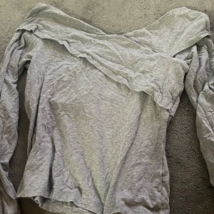Grå offshoulder topp - Säljer en snygg grå offshoulder topp som är perfekt för både vardag och fest. Den har långa ärmar och är gjord i ett mjukt och bekvämt material. Passar bra till jeans eller kjol för en stilren look.