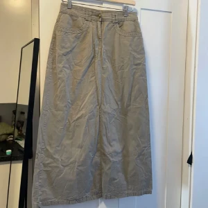 Beige långkjol med fickor - Säljer en superfin beige långkjol som är perfekt för både vardag och lite mer uppklädda tillfällen. Kjolen har en klassisk design med praktiska fickor både fram och bak, vilket ger den en avslappnad men ändå stilren look. Den är gjord i ett bekvämt bomullsmaterial och har en knapp och dragkedja framtill för enkel påklädning. Passar perfekt till en stickad tröja eller en enkel t-shirt!