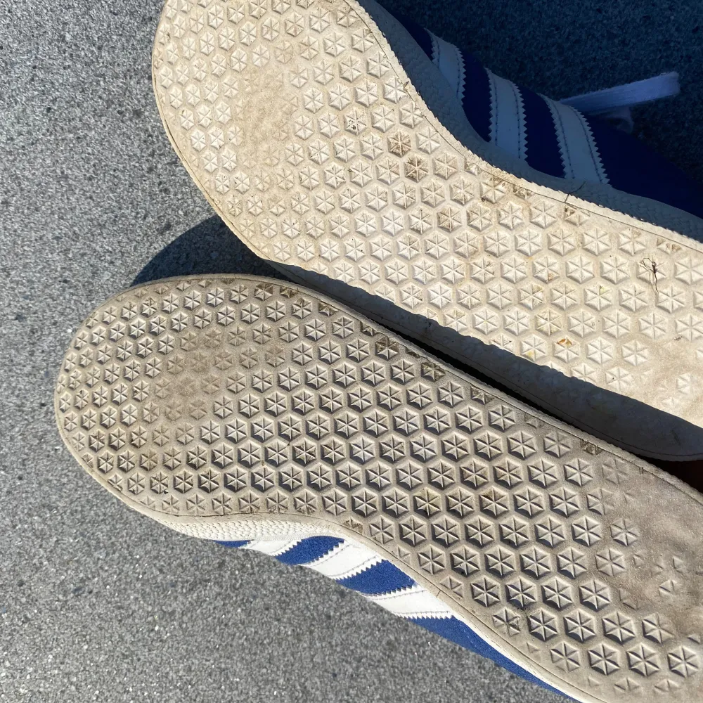 Säljer ett par klassiska blå Adidas Gazelle sneakers i mocka med vita detaljer. Skorna har den ikoniska tre-randiga designen och vit sula. De är i mycket bra skick med lite slitage på sulan. Perfekta för både vardag och fest! . Skor.