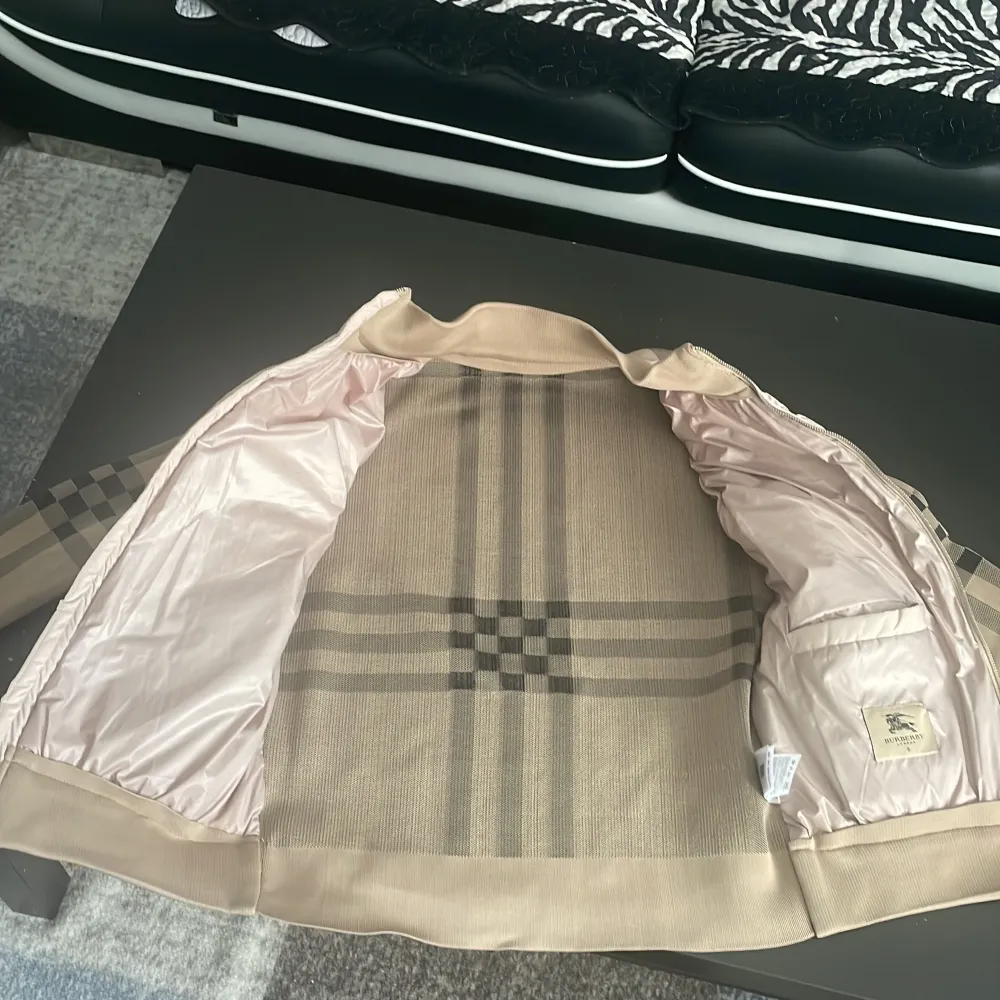 Säljer en snygg beige quiltad jacka från Burberry. Den har ett klassiskt rutigt mönster på ärmarna och baksidan, och en dragkedja framtill. Jackan är perfekt för höst och vår, med en stilren look som passar både till vardags och fest. Den är i nyskick och redo för en ny ägare!. Jackor.