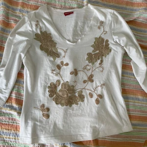 Vit långärmad topp från Taifun - Säljer en vit långärmad topp från Taifun. Den har en v-ringad hals och är dekorerad med vackra broderade blommor i beige. Perfekt för både vardag och festliga tillfällen. Toppen är i bra skick och väldigt bekväm att bära.