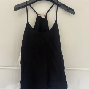 Svart linnetopp från H&M - Säljer en svart linnetopp från H&M i storlek XS. Toppen är ärmlös med smala axelband och en enkel design. Perfekt för sommaren eller som ett basplagg i garderoben. Använd men i bra skick.